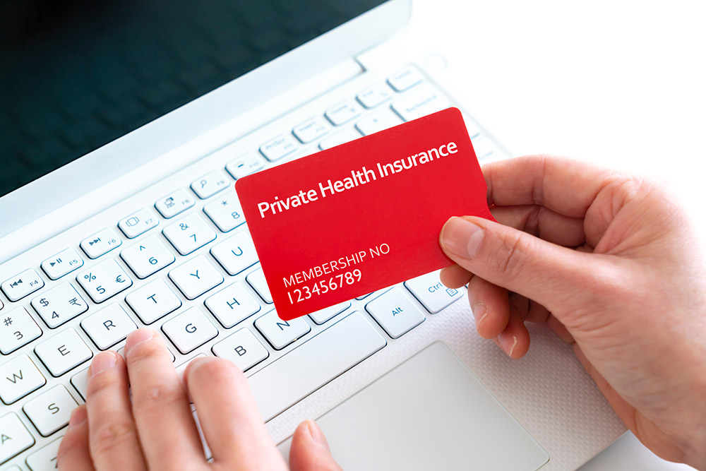 Close-up of woman holding a private health insurance card with laptop concept
