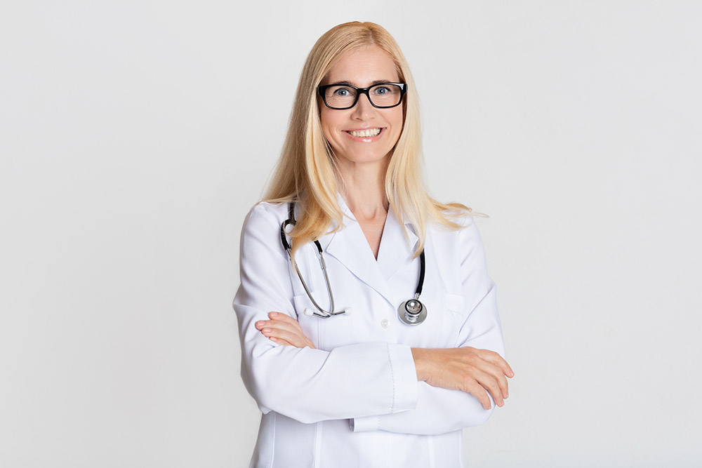 Smiling medical physician doctor posing with crossed arms on grey studio background