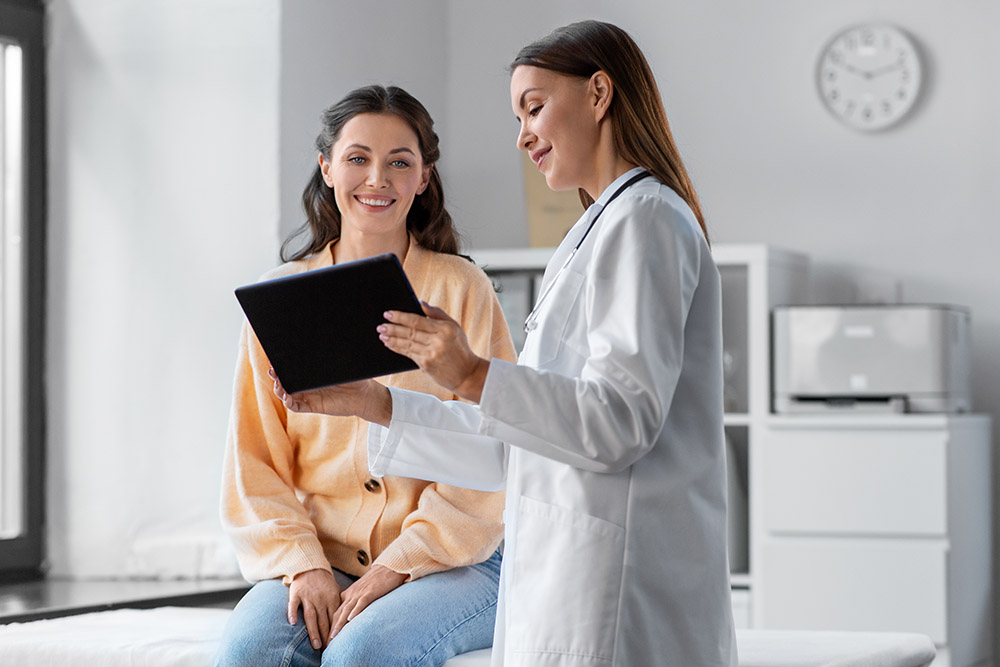 female doctor with tablet pc computer talking to smiling woman patient at hospital