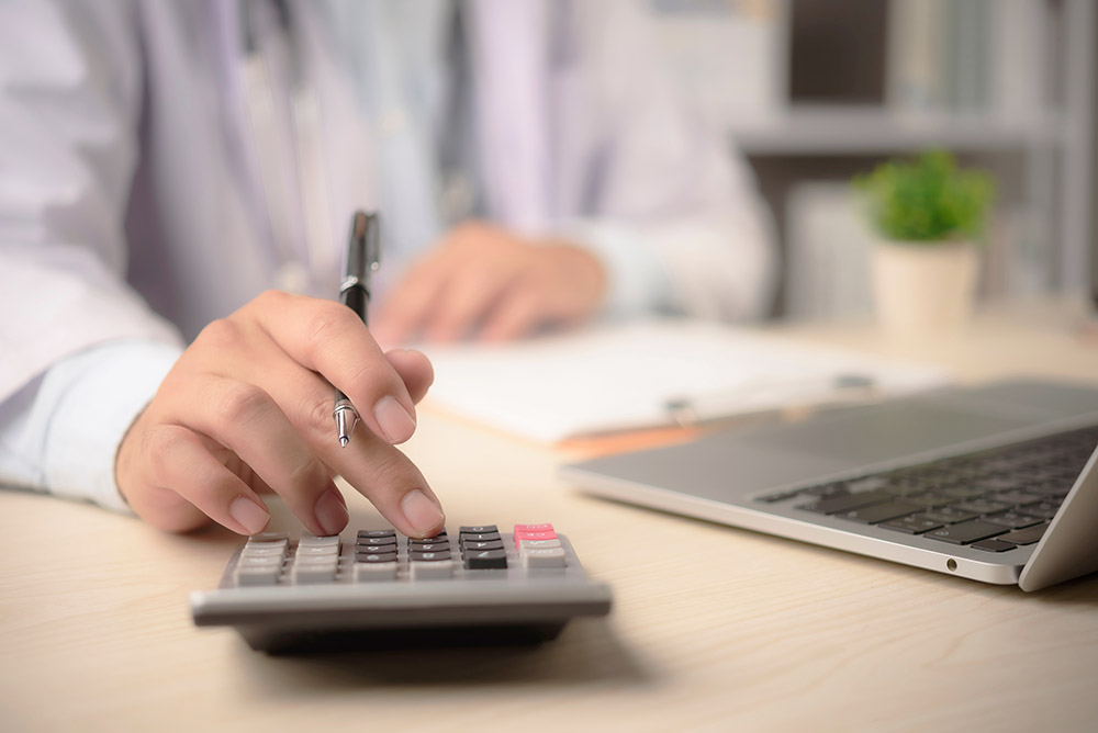 Doctor calculates medical billing at office desk with calculator laptop paperwork for insurance claim
