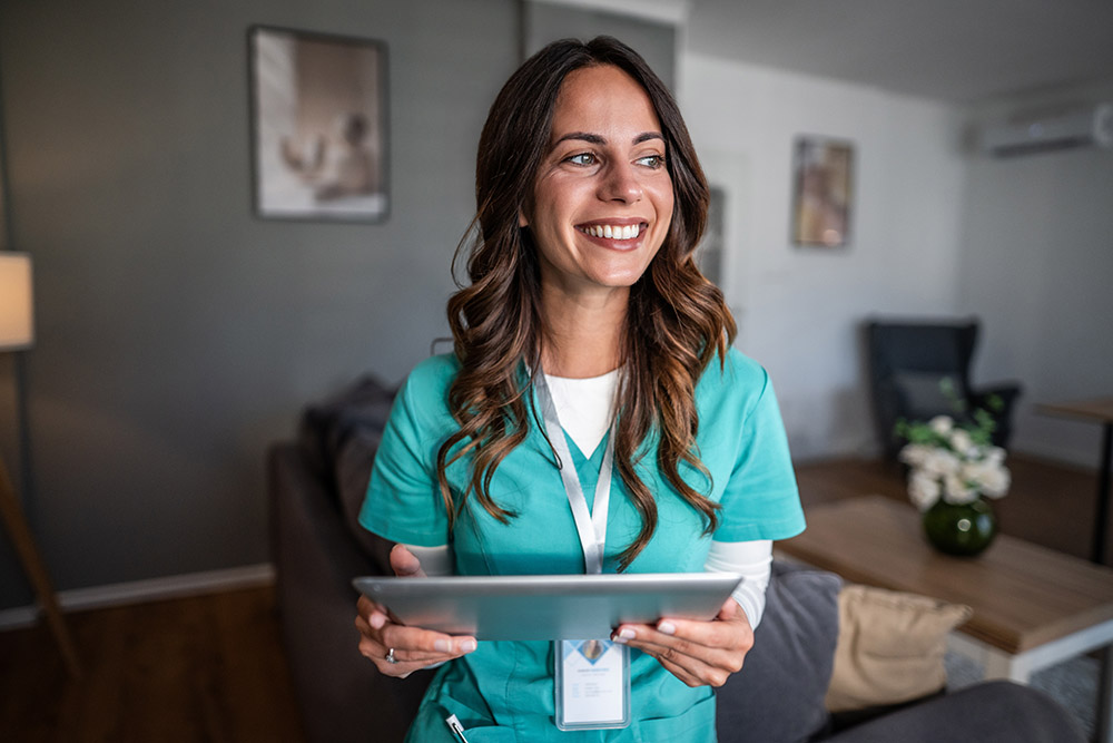 Smiling nurse holding a digital tablet in a residential setting, representing dedicated healthcare professional using technology for home care and patient assistance