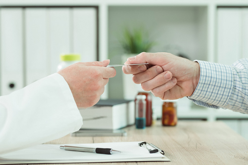 Doctor taking medical insurance card from patient in office during scheduled checkup