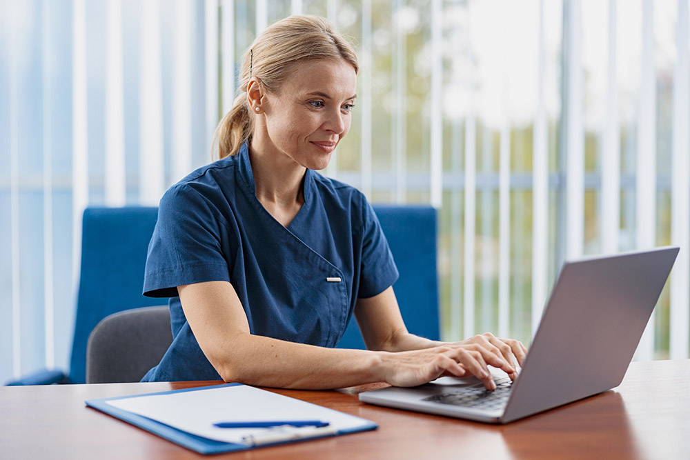 Smiling doctor working laptop during appointment in her medical office.
