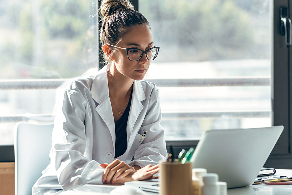 Shot of female doctor talking while explaining medical treatment to patient through a video call with laptop and earphones in the consultation.