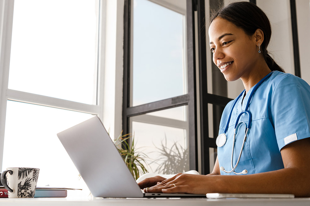 Black woman doctor working with laptop while sitting at table in home
