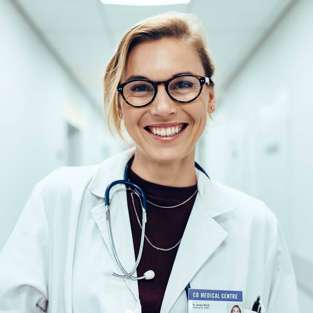 Portrait of happy young female doctor standing in hospital corridor
